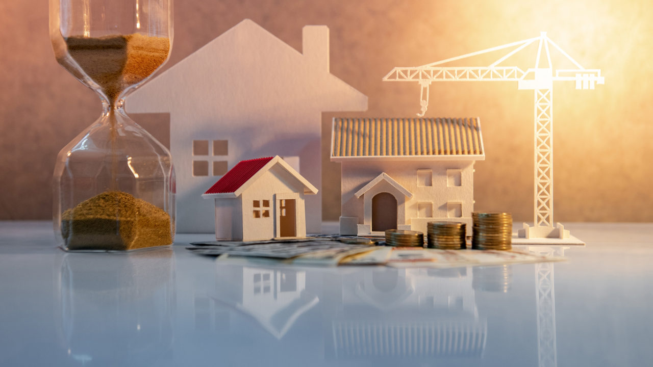 Real estate or property development. Construction business investment concept. Home mortgage loan rate. Coin stack on international banknotes with hourglasses, house and crane models on the table.